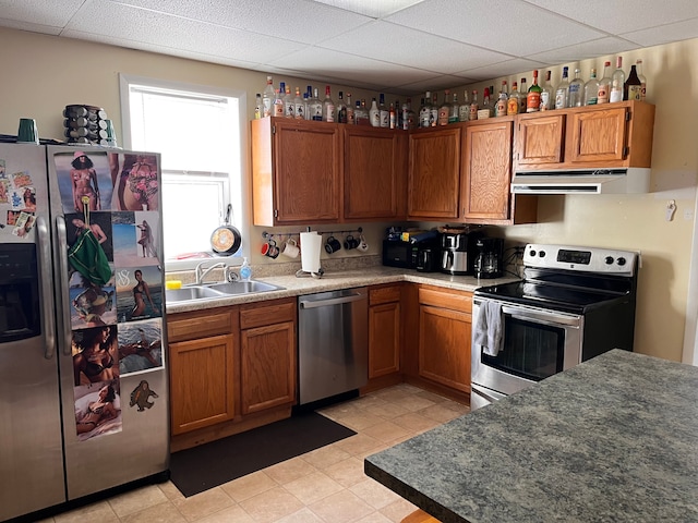 kitchen featuring appliances with stainless steel finishes, brown cabinets, a paneled ceiling, under cabinet range hood, and a sink