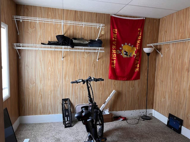 workout room with carpet, a drop ceiling, wooden walls, and baseboards