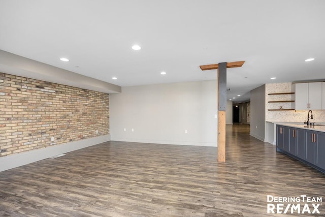 unfurnished living room featuring dark wood-style floors, brick wall, a sink, and recessed lighting