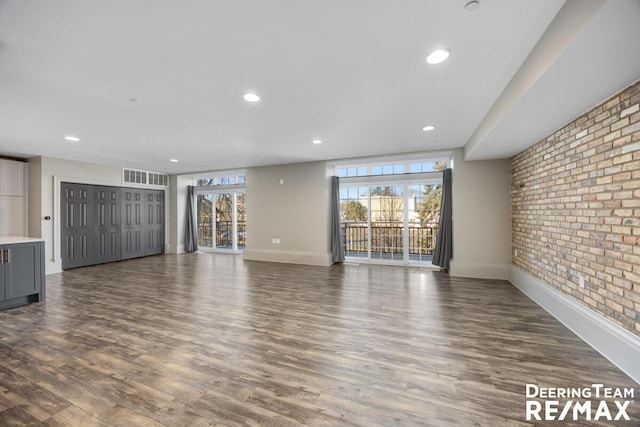 unfurnished living room featuring recessed lighting, brick wall, wood finished floors, visible vents, and baseboards