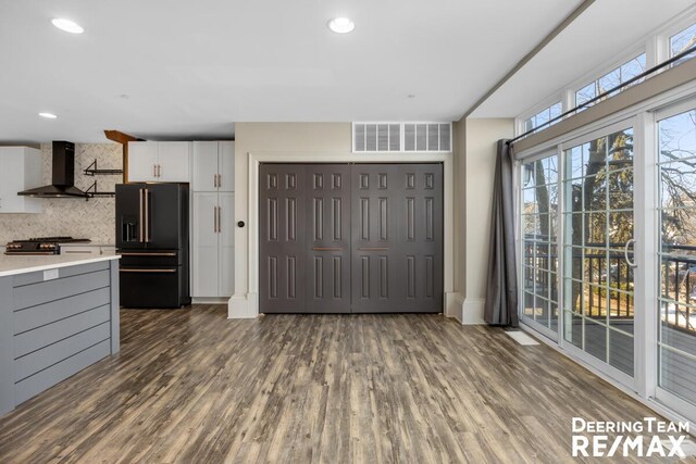 kitchen featuring dark wood-style flooring, light countertops, visible vents, black refrigerator with ice dispenser, and wall chimney exhaust hood