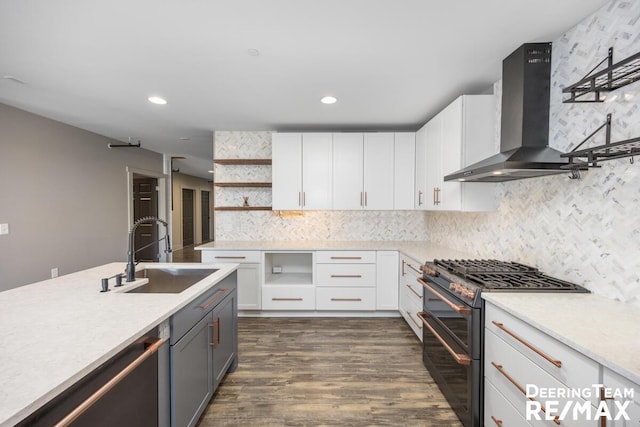 kitchen with range with two ovens, open shelves, light countertops, a sink, and wall chimney range hood