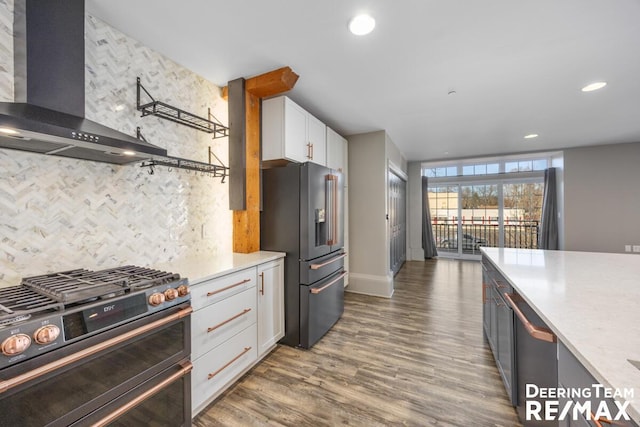 kitchen with stainless steel appliances, light countertops, white cabinetry, wall chimney range hood, and wood finished floors