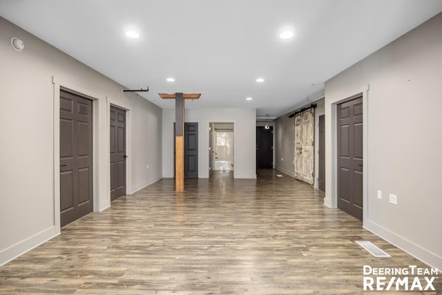 unfurnished room featuring light wood finished floors, a barn door, baseboards, and recessed lighting