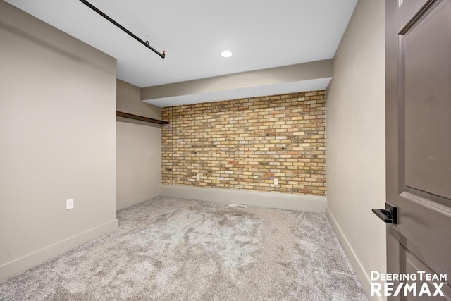 spare room featuring carpet, baseboards, and brick wall