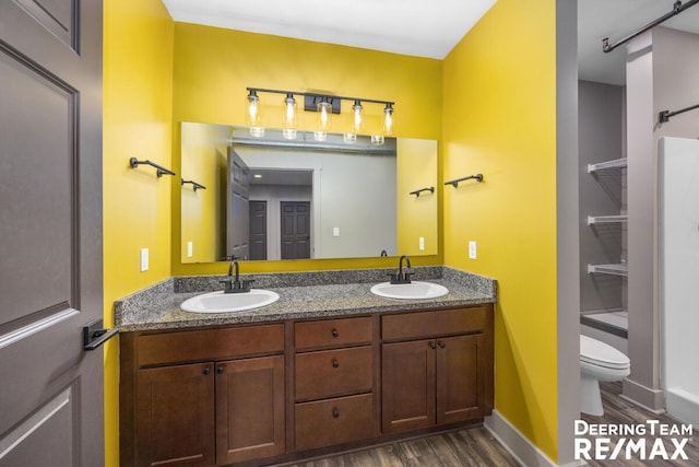 bathroom featuring toilet, double vanity, a sink, and wood finished floors