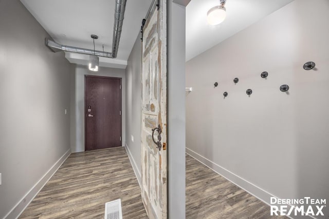 hall featuring visible vents, baseboards, wood finished floors, and a barn door