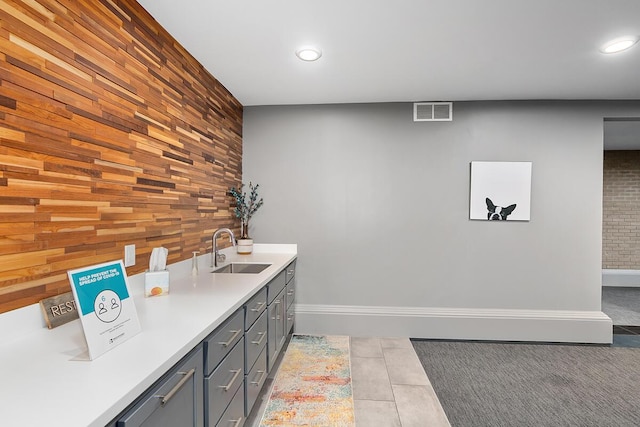 bathroom featuring tile patterned flooring, an accent wall, wood walls, a sink, and visible vents