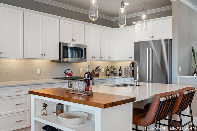 kitchen featuring crown molding, a center island with sink, open shelves, butcher block counters, and appliances with stainless steel finishes