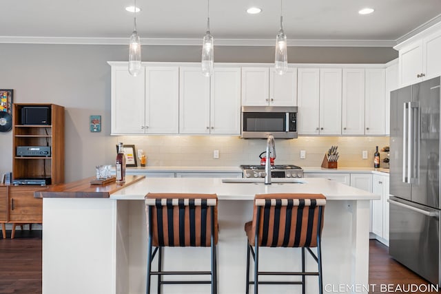 kitchen with dark wood-style floors, crown molding, backsplash, appliances with stainless steel finishes, and a kitchen island with sink