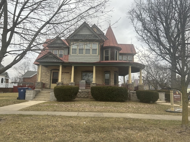 victorian home featuring covered porch, brick siding, metal roof, and a standing seam roof