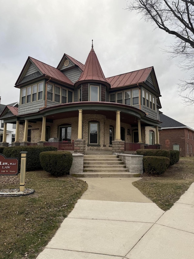 victorian-style house featuring a porch, a standing seam roof, brick siding, and metal roof