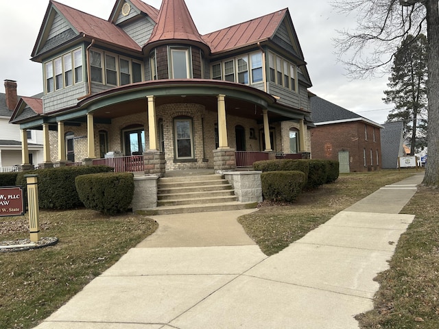 victorian house featuring a standing seam roof, metal roof, a porch, and brick siding