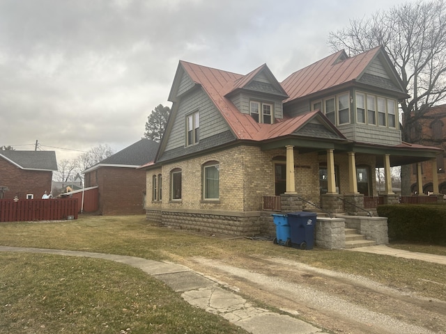 view of front of home featuring metal roof, a porch, brick siding, a front lawn, and a standing seam roof