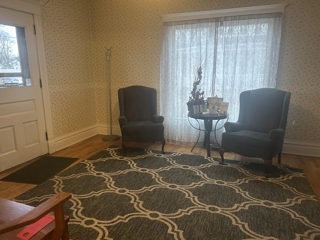 living area featuring wallpapered walls, baseboards, and wood finished floors