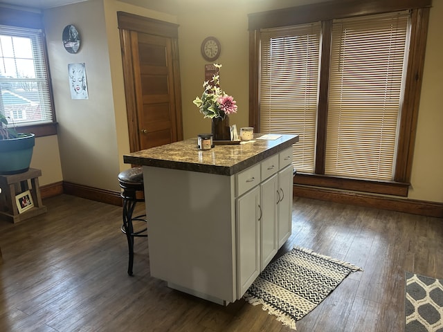 kitchen featuring dark wood-style floors, dark countertops, white cabinets, a kitchen island, and baseboards