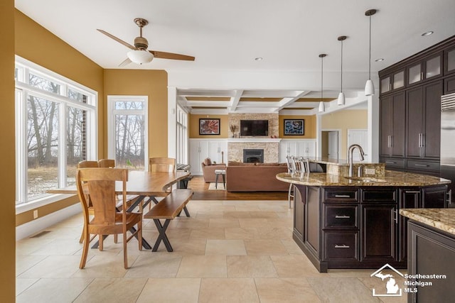 kitchen with coffered ceiling, glass insert cabinets, a sink, a fireplace, and beam ceiling