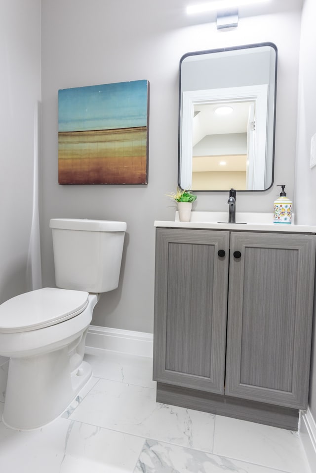 half bath with baseboards, toilet, marble finish floor, and vanity