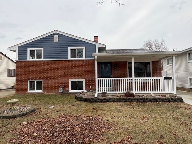 exterior space featuring a front yard, a chimney, a porch, and brick siding