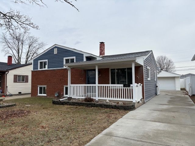 tri-level home with a porch, a garage, brick siding, an outdoor structure, and a chimney