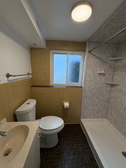 bathroom featuring tile walls, toilet, a tile shower, vanity, and tile patterned flooring