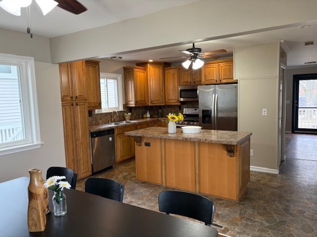 kitchen featuring stainless steel appliances, brown cabinetry, stone finish flooring, a sink, and a kitchen island