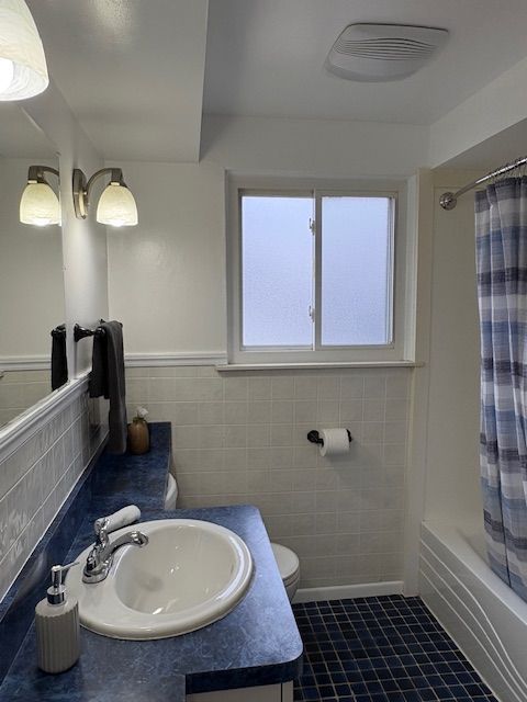 full bath with toilet, tile walls, vanity, tile patterned floors, and shower / bath combo