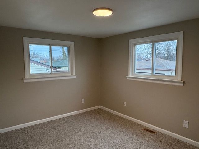 carpeted empty room featuring a healthy amount of sunlight, visible vents, and baseboards