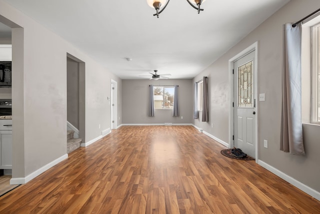 unfurnished living room with stairway, baseboards, and wood finished floors