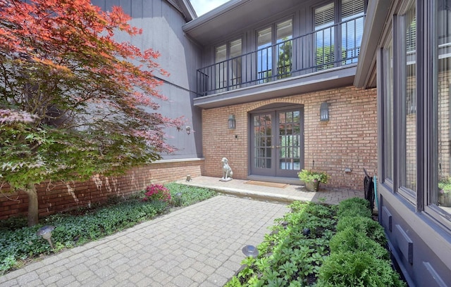 entrance to property featuring french doors, a balcony, and brick siding