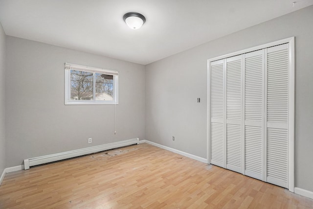 unfurnished bedroom featuring light wood-style floors, baseboards, baseboard heating, and a closet