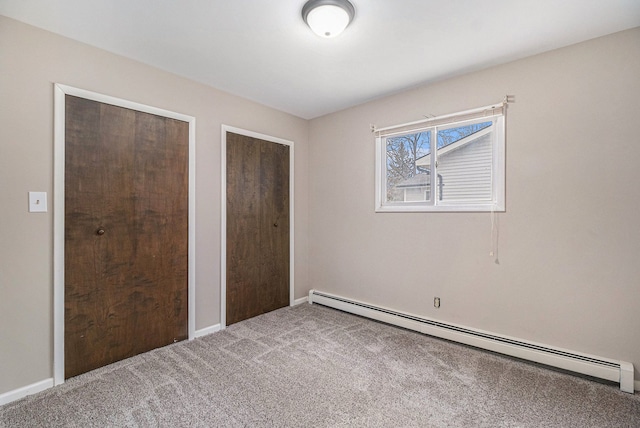 unfurnished bedroom featuring a baseboard heating unit, carpet floors, baseboards, and two closets