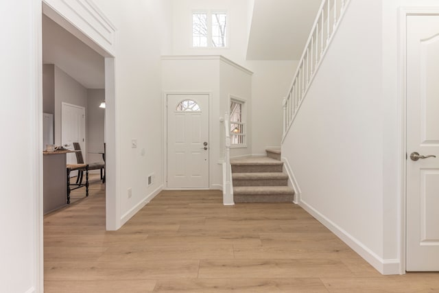 foyer with stairway, baseboards, light wood-type flooring, and a towering ceiling