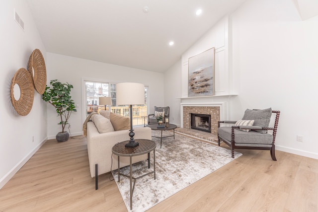 living room featuring visible vents, baseboards, vaulted ceiling, light wood-style floors, and a brick fireplace