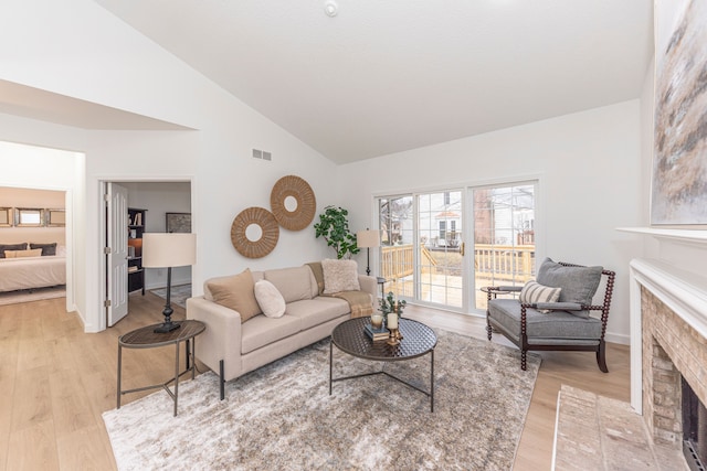 living area with a fireplace, visible vents, light wood finished floors, and high vaulted ceiling