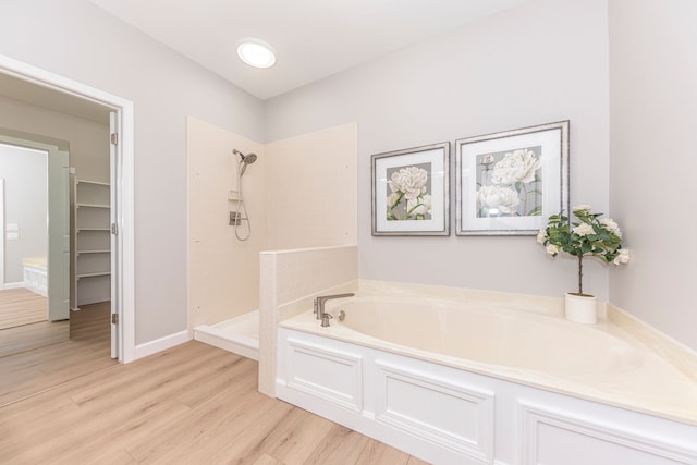 bathroom featuring wood finished floors, baseboards, tiled shower, and a bath