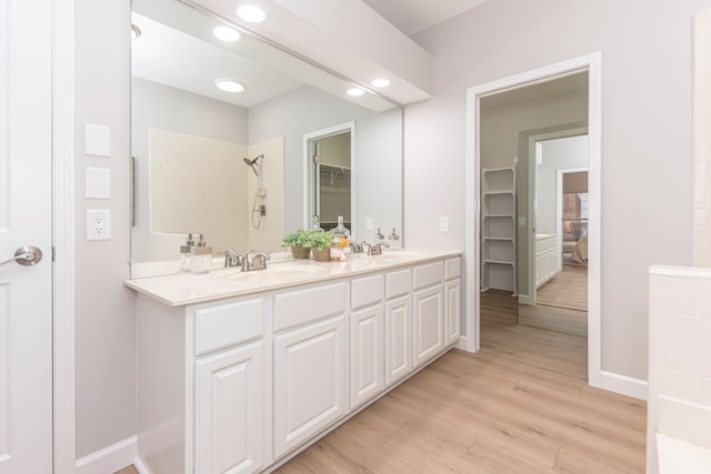 bathroom featuring wood finished floors, double vanity, recessed lighting, a sink, and walk in shower