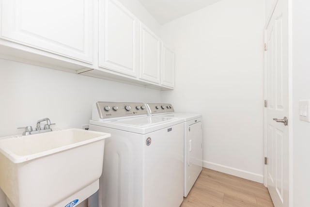 clothes washing area with baseboards, cabinet space, separate washer and dryer, a sink, and light wood-type flooring