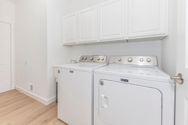 laundry room featuring light wood finished floors, washing machine and dryer, cabinet space, and baseboards