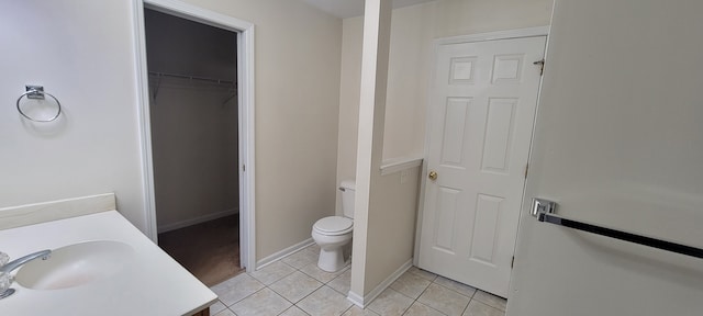 bathroom featuring baseboards, toilet, tile patterned flooring, a spacious closet, and a sink