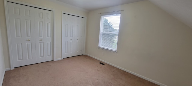 unfurnished bedroom with lofted ceiling, light carpet, visible vents, baseboards, and multiple closets