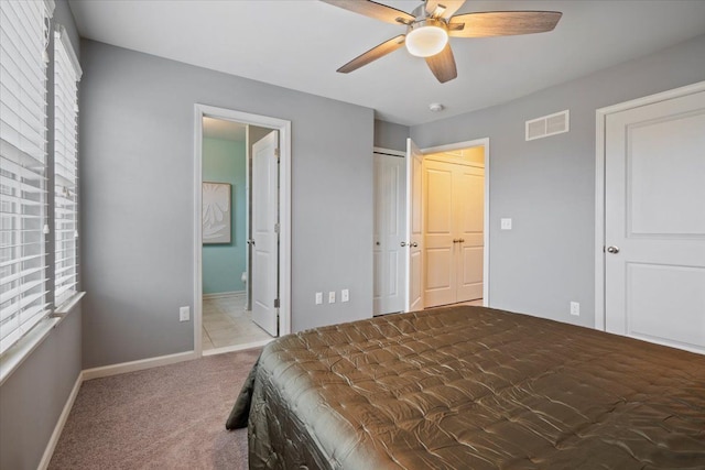 carpeted bedroom with ensuite bathroom, a ceiling fan, visible vents, and baseboards