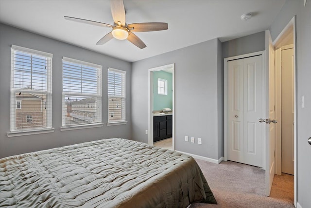 bedroom featuring a closet, light carpet, ceiling fan, ensuite bath, and baseboards