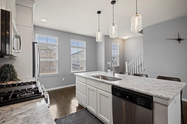 kitchen featuring baseboards, white cabinets, light stone counters, stainless steel appliances, and a sink