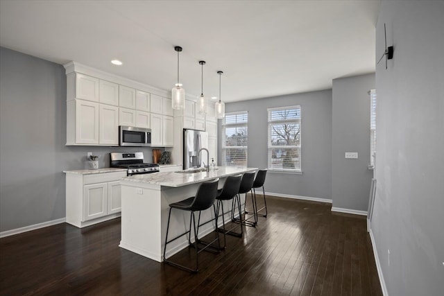 kitchen with a center island with sink, baseboards, dark wood-style floors, stainless steel appliances, and white cabinetry