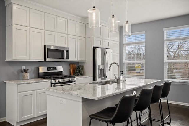 kitchen with stainless steel appliances, a center island with sink, a sink, and white cabinetry