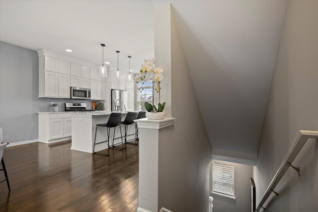 kitchen featuring appliances with stainless steel finishes, white cabinets, dark wood-type flooring, and a breakfast bar area