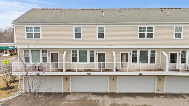 rear view of property featuring an attached garage and roof with shingles