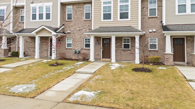 view of property featuring a shingled roof, a front yard, and brick siding