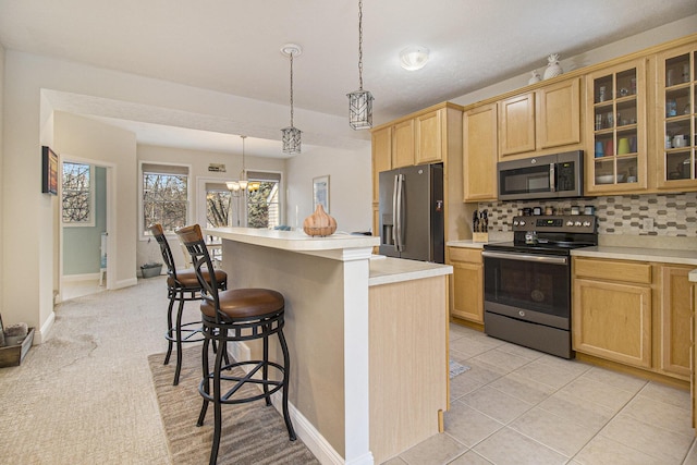 kitchen featuring stainless steel appliances, light countertops, glass insert cabinets, light brown cabinets, and a kitchen breakfast bar